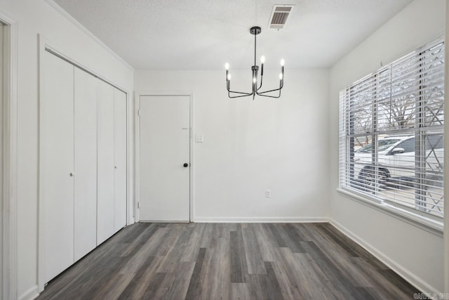 unfurnished dining area featuring dark hardwood / wood-style flooring, a chandelier, and a textured ceiling