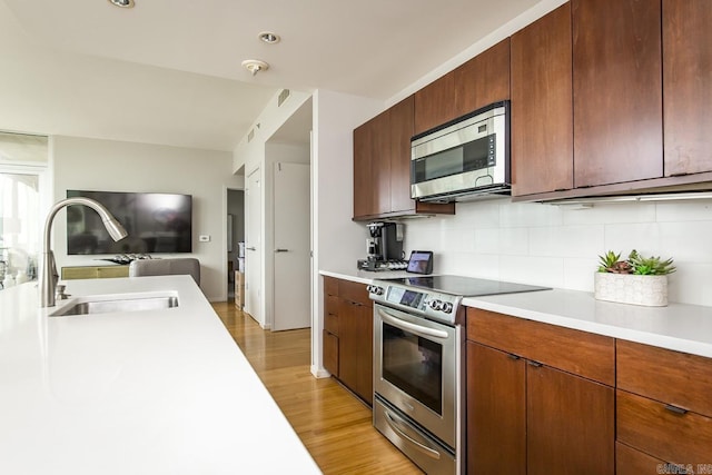 kitchen with tasteful backsplash, sink, stainless steel appliances, and light wood-type flooring