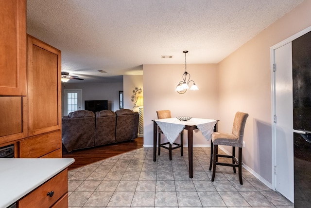 dining space with ceiling fan with notable chandelier, a textured ceiling, and light tile patterned floors