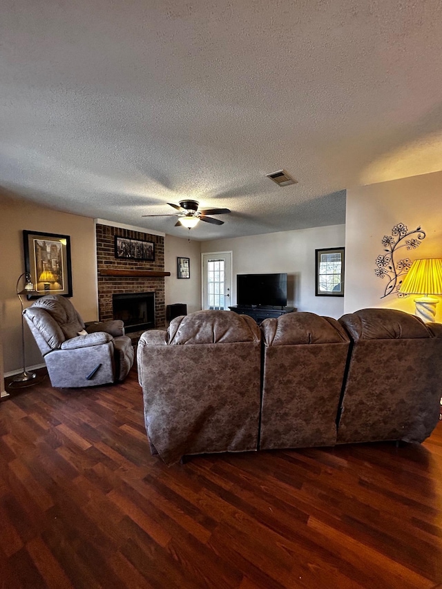 living room with ceiling fan, a brick fireplace, dark wood-type flooring, and a textured ceiling