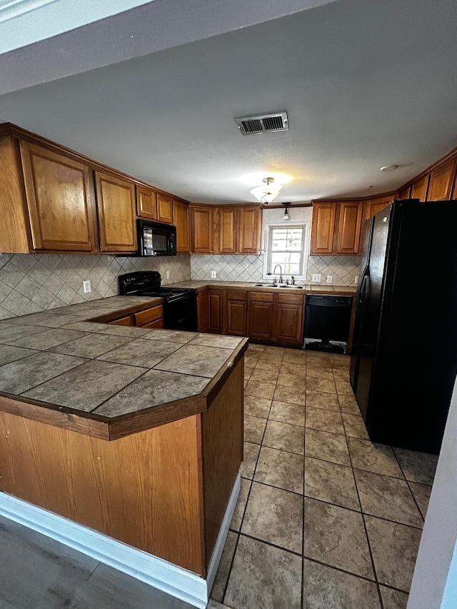 kitchen with kitchen peninsula, sink, decorative backsplash, dark tile patterned floors, and black appliances