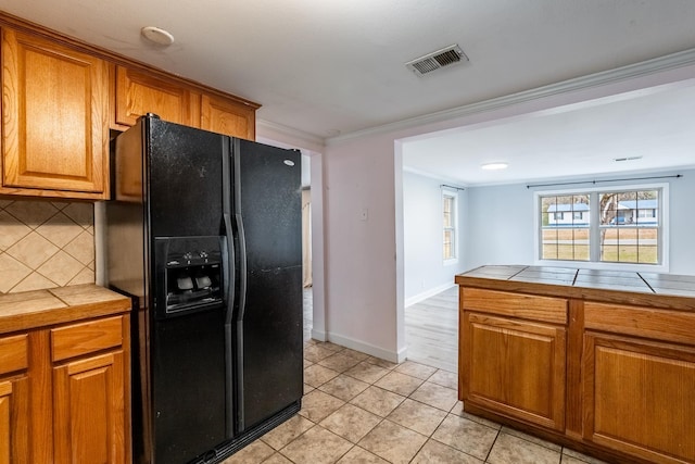 kitchen featuring tasteful backsplash, tile counters, ornamental molding, and black fridge