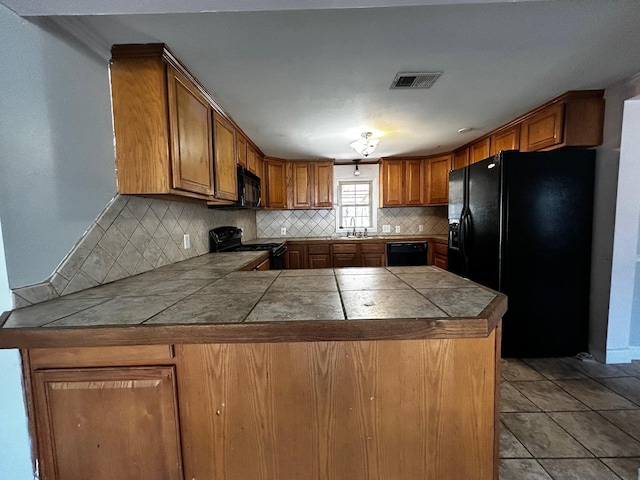 kitchen featuring black appliances, tile countertops, backsplash, and kitchen peninsula