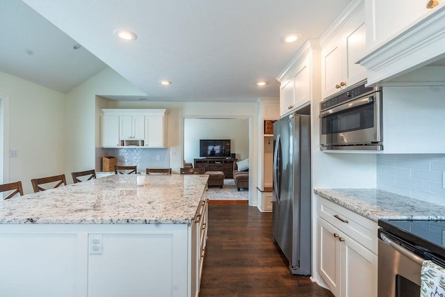 kitchen featuring a breakfast bar, stainless steel refrigerator, white cabinets, a center island, and light stone counters