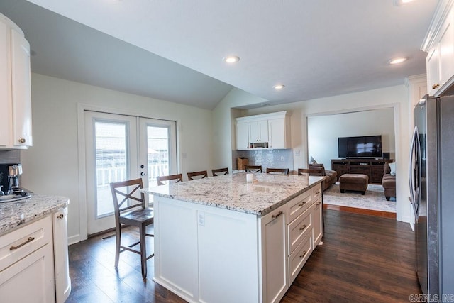 kitchen with stainless steel refrigerator, white cabinetry, a kitchen island, and a breakfast bar area