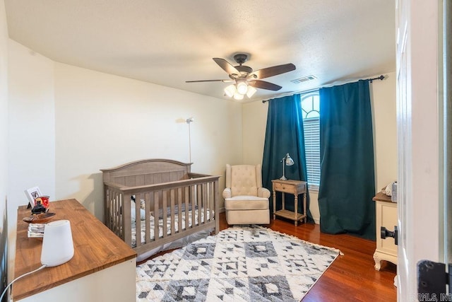 bedroom with dark hardwood / wood-style flooring, a nursery area, and ceiling fan