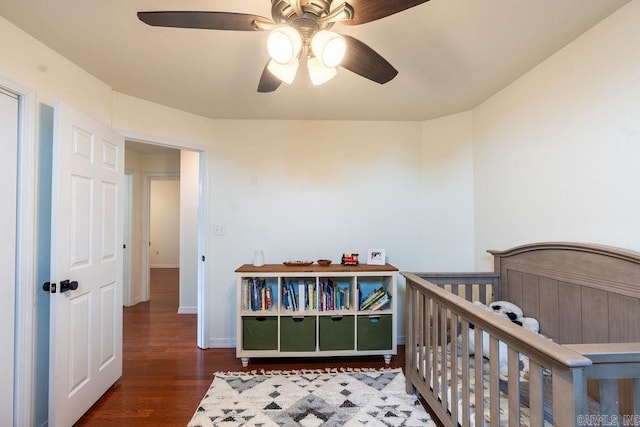 bedroom featuring a crib, dark wood-type flooring, and ceiling fan