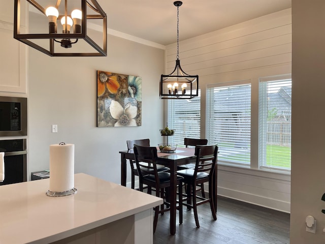 dining space with dark wood-type flooring, wooden walls, crown molding, and a notable chandelier