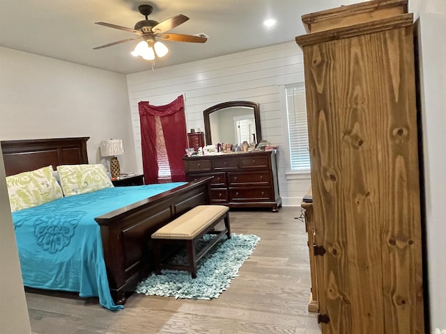 bedroom featuring ceiling fan, light hardwood / wood-style floors, and wood walls