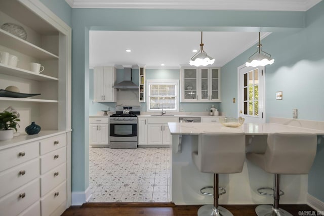 kitchen featuring wall chimney exhaust hood, a kitchen bar, white cabinetry, hanging light fixtures, and appliances with stainless steel finishes