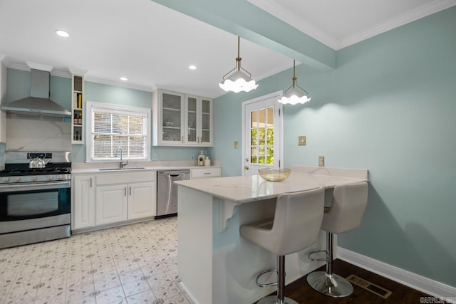 kitchen with a breakfast bar, white cabinetry, sink, stainless steel appliances, and wall chimney exhaust hood