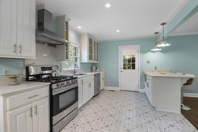 kitchen with wall chimney range hood, a breakfast bar, appliances with stainless steel finishes, white cabinetry, and decorative light fixtures