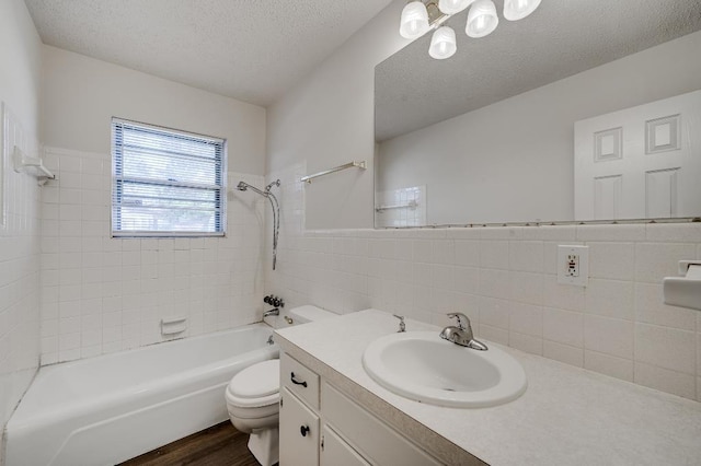 full bathroom with tiled shower / bath, tile walls, vanity, toilet, and a textured ceiling