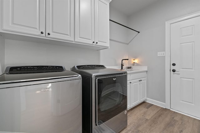 clothes washing area featuring cabinets, sink, washer and dryer, and light hardwood / wood-style flooring