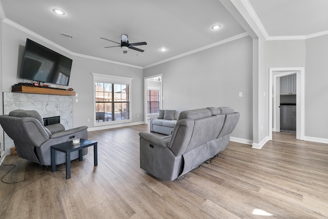 living room with a stone fireplace, light hardwood / wood-style flooring, and ornamental molding