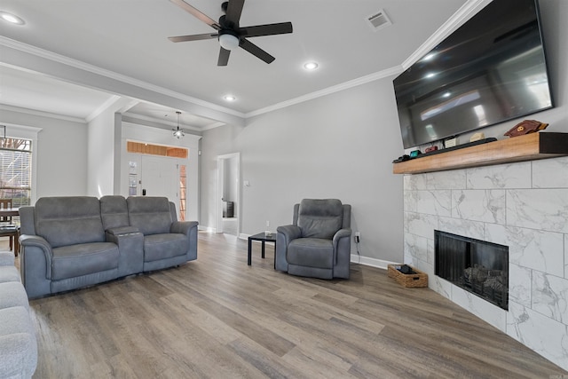 living room featuring a tiled fireplace, ornamental molding, hardwood / wood-style floors, and ceiling fan