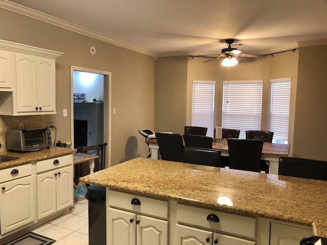 kitchen featuring ceiling fan, light stone countertops, ornamental molding, white cabinets, and light tile patterned flooring