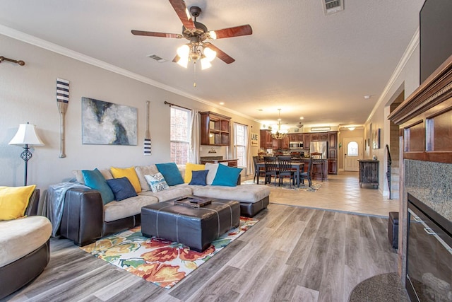 living room with crown molding, ceiling fan with notable chandelier, and light wood-type flooring