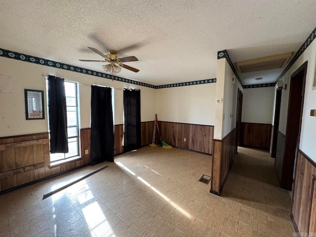 unfurnished room featuring ceiling fan, wooden walls, and a textured ceiling