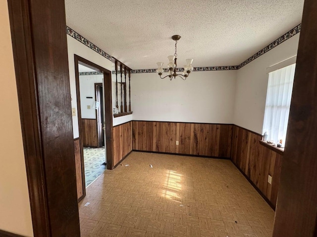 unfurnished dining area featuring wooden walls, a chandelier, and a textured ceiling