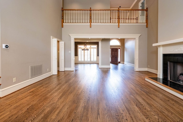 unfurnished living room with an inviting chandelier, a towering ceiling, dark hardwood / wood-style flooring, and a tile fireplace