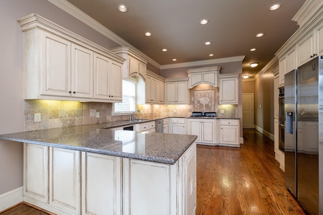 kitchen featuring crown molding, wood-type flooring, appliances with stainless steel finishes, kitchen peninsula, and decorative backsplash