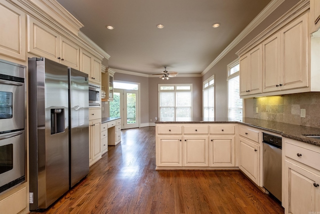 kitchen with dark wood-type flooring, ornamental molding, appliances with stainless steel finishes, kitchen peninsula, and backsplash