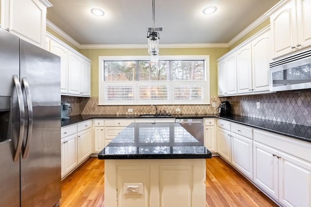 kitchen featuring crown molding, appliances with stainless steel finishes, white cabinetry, hanging light fixtures, and a kitchen island