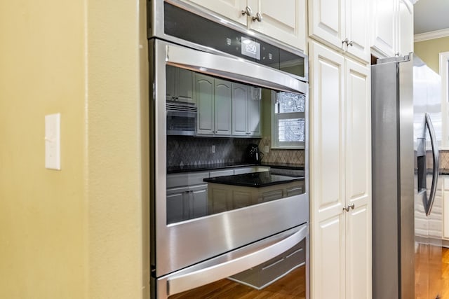 kitchen featuring ornamental molding, stainless steel appliances, wood-type flooring, and white cabinets