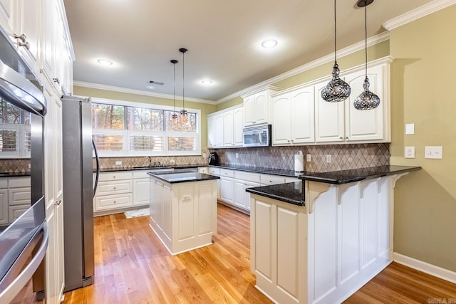 kitchen with white cabinetry, hanging light fixtures, stainless steel appliances, a center island, and kitchen peninsula