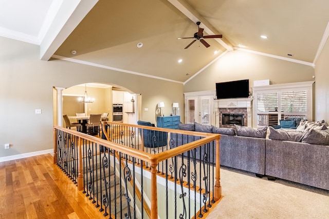 living room featuring vaulted ceiling with beams, a tiled fireplace, ornamental molding, ceiling fan, and light hardwood / wood-style floors