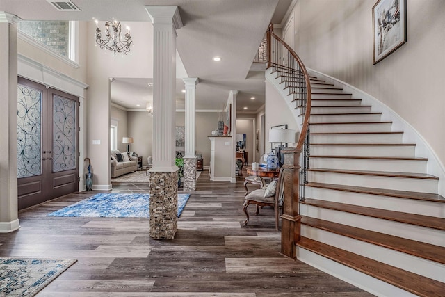 entryway with a towering ceiling, a notable chandelier, dark hardwood / wood-style floors, and ornate columns