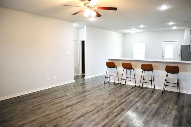 kitchen featuring stainless steel fridge, a breakfast bar area, ceiling fan, dark hardwood / wood-style floors, and kitchen peninsula