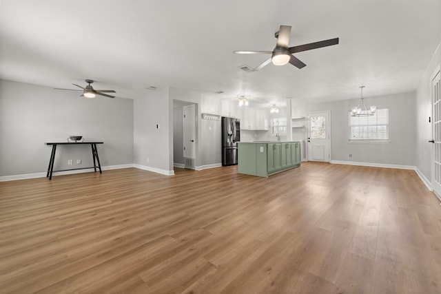 unfurnished living room featuring sink, ceiling fan with notable chandelier, and light wood-type flooring