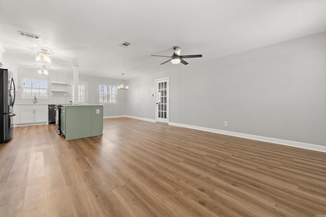 unfurnished living room featuring ceiling fan with notable chandelier and light hardwood / wood-style floors