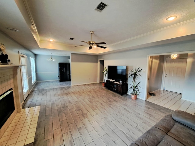 unfurnished living room with ceiling fan with notable chandelier, a fireplace, a tray ceiling, crown molding, and a textured ceiling