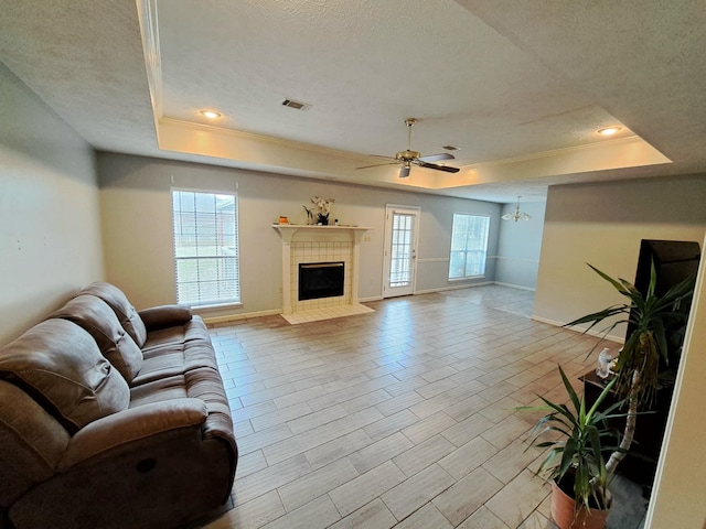 living room featuring a tile fireplace, a textured ceiling, and a tray ceiling