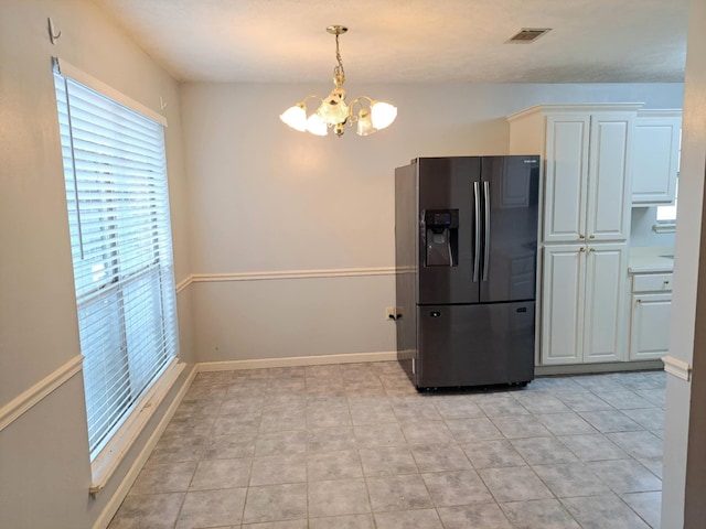 kitchen with light tile patterned flooring, pendant lighting, white cabinets, stainless steel fridge, and a chandelier