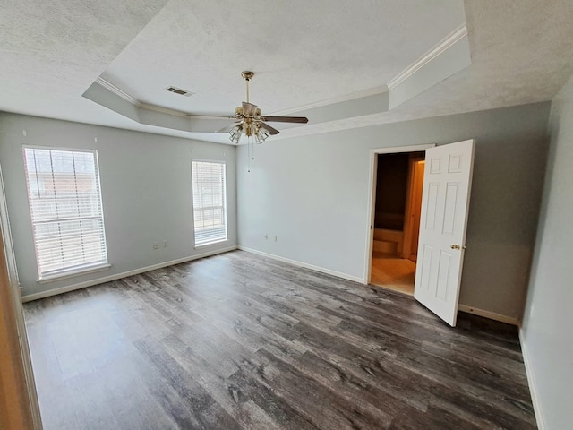 empty room with dark hardwood / wood-style floors, ornamental molding, ceiling fan, a tray ceiling, and a textured ceiling