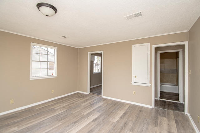 empty room with ornamental molding, a textured ceiling, and light hardwood / wood-style floors