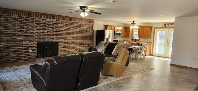 living room with sink, ceiling fan, brick wall, a brick fireplace, and french doors