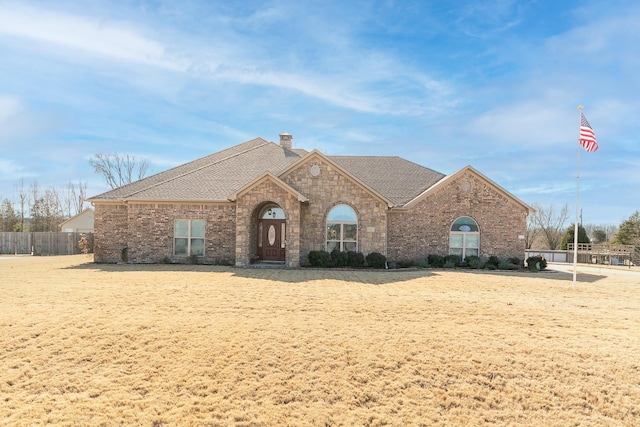 view of front of property with roof with shingles, brick siding, a chimney, and fence