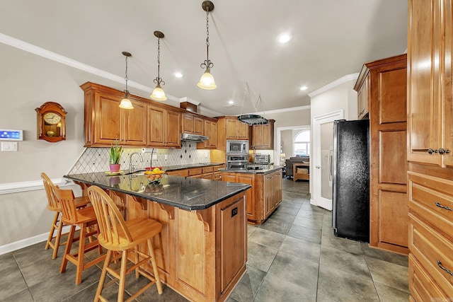 kitchen featuring a peninsula, appliances with stainless steel finishes, brown cabinetry, and under cabinet range hood