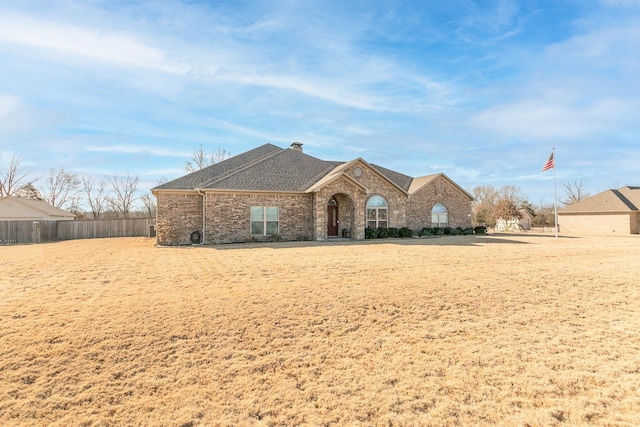 french country home featuring a shingled roof, a chimney, fence, and brick siding