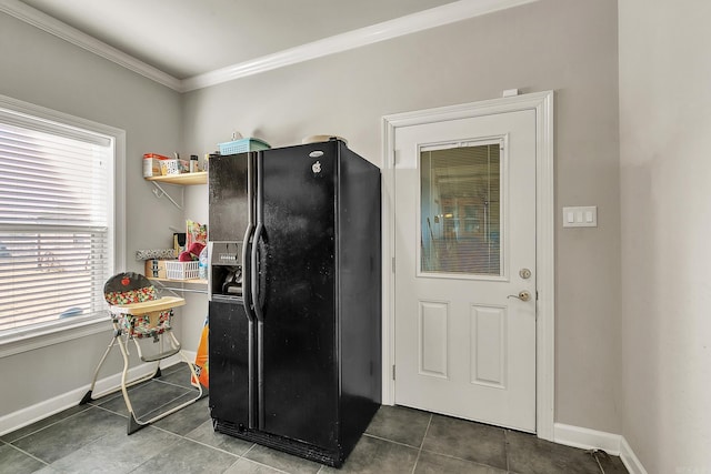 kitchen with dark tile patterned flooring, ornamental molding, black fridge, and baseboards