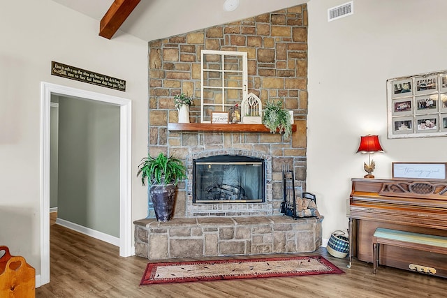 living area with visible vents, vaulted ceiling with beams, a fireplace, and wood finished floors