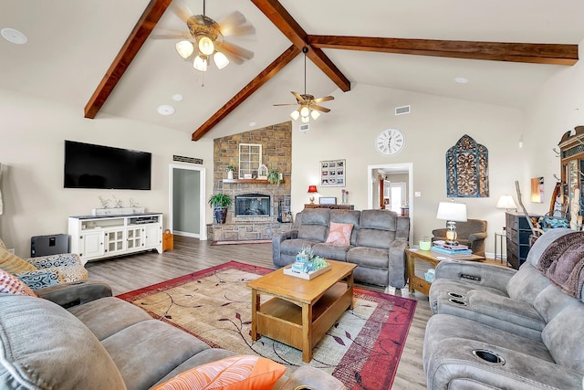 living room with beam ceiling, visible vents, a stone fireplace, wood finished floors, and high vaulted ceiling