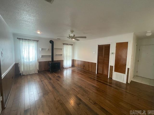 unfurnished living room with ceiling fan, dark hardwood / wood-style floors, a textured ceiling, and a wood stove