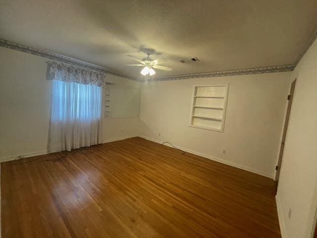 spare room featuring built in shelves, ceiling fan, dark hardwood / wood-style floors, and crown molding