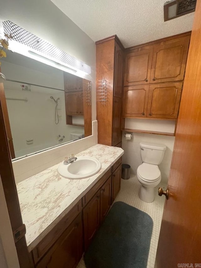 bathroom with toilet, a shower, a textured ceiling, vanity, and tile patterned flooring